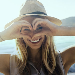 Woman in sunshine making heart shape with hands over her face