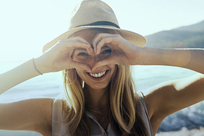 Woman in sunshine making heart shape with hands over her face