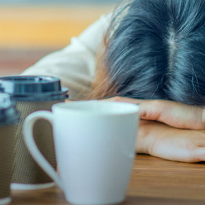 Stressed woman with head on desk and coffee cups in foreground