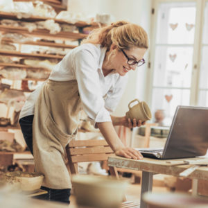 Potter entrepreneur using laptop in workshop - super for self-employed concept