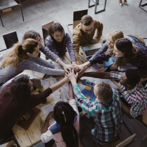 Top view of business team working at trendy loft office. Young mixed race group of people puts palm together on centre, crowdfunding concept