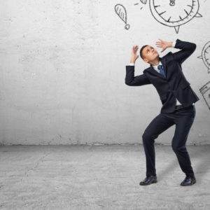 Businessman shielding himself with his hands from the drawings of calendars and clocks on the grey wall. Business and time-management. Organising and planning. Productivity and efficiency.