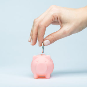 Female hand putting a coin into piggy bank, saving while young